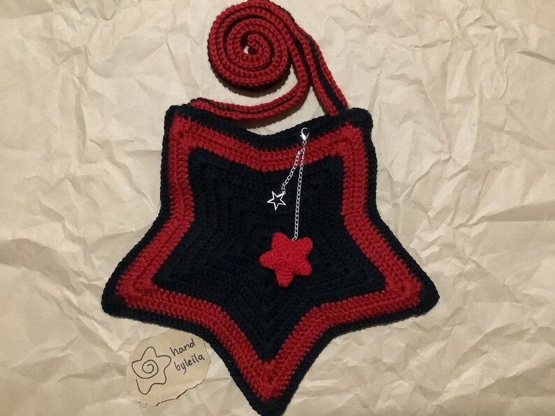 May include: A black and red crocheted star-shaped bag with a red star charm and a silver chain. The bag has a red crocheted strap. The tag says "hand by leila".
