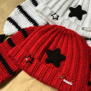 May include: Two crocheted hats with black and white stripes. One hat is red with a black star and the other is white with a black star. Both hats have a safety pin with a number on it.