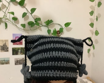 May include: A black and gray striped crocheted hat with two star-shaped embellishments. The hat has a safety pin attached to it.