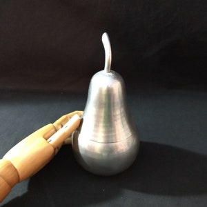 May include: A silver pear-shaped sugar bowl with a wooden hand reaching towards it.