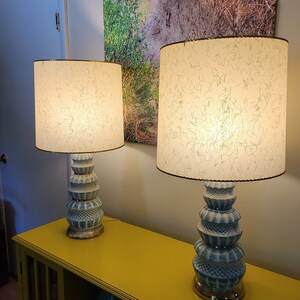 May include: Two blue and white ceramic table lamps with white lampshades with a green pattern. The lamps are on a yellow table.