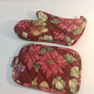 May include: A set of two quilted pot holders with a red, green, and white floral pattern. The pot holders are made of fabric and have a quilted design.