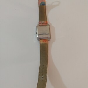 May include: A silver square watch with a brown leather band. The watch face has a white background with black text that reads "Alberto Fiore" and "T.I.M.E.  MADE IN CHINA".