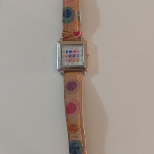 May include: A silver square watch with a white face and colorful polka dot pattern on the band.
