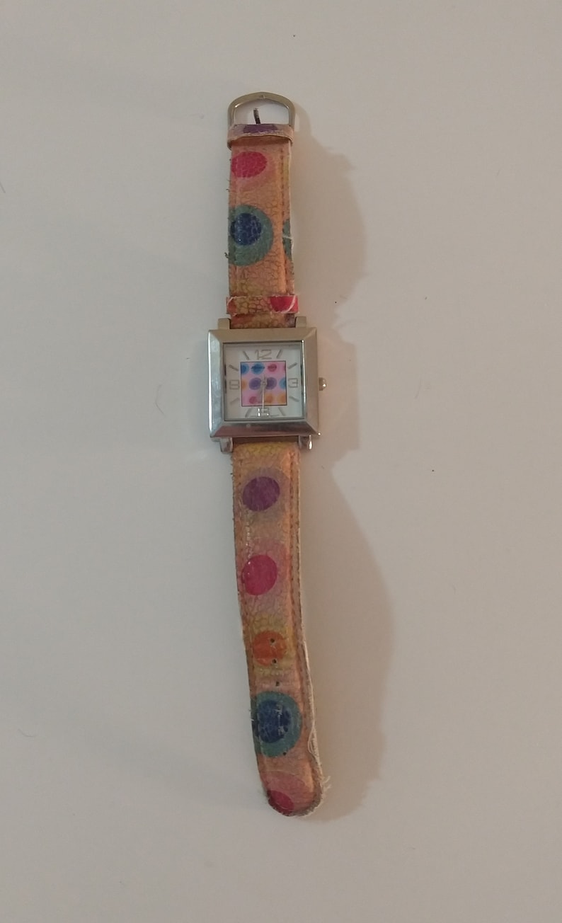 May include: A silver square watch with a white face and colorful polka dot pattern on the band.