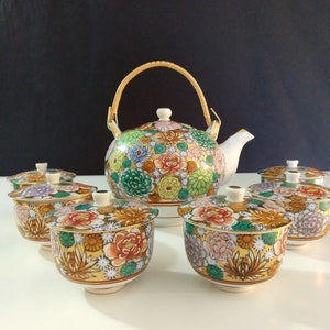 May include: A white porcelain teapot with a bamboo handle and floral pattern, along with five matching teacups and saucers. The teapot and cups are decorated with colorful flowers and leaves.