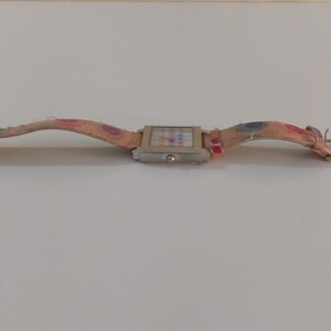 May include: A silver square watch with a colorful patterned band. The band is made of fabric and has a buckle closure.