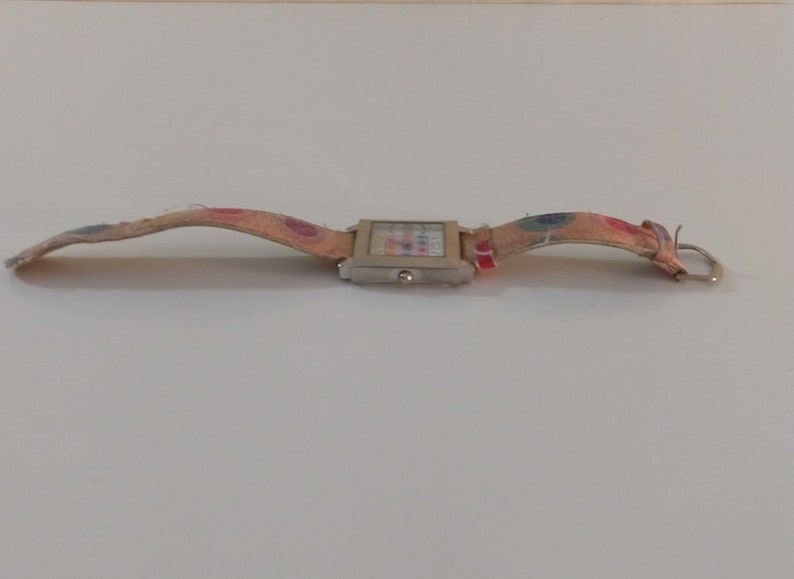 May include: A silver square watch with a colorful patterned band. The band is made of fabric and has a buckle closure.
