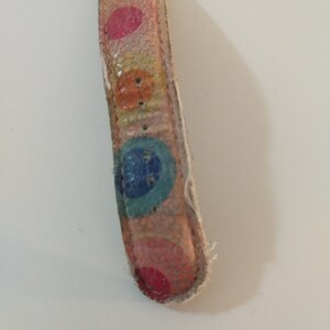 May include: A close-up of a watch strap with a colorful polka dot pattern. The strap is made of leather and has a silver buckle.