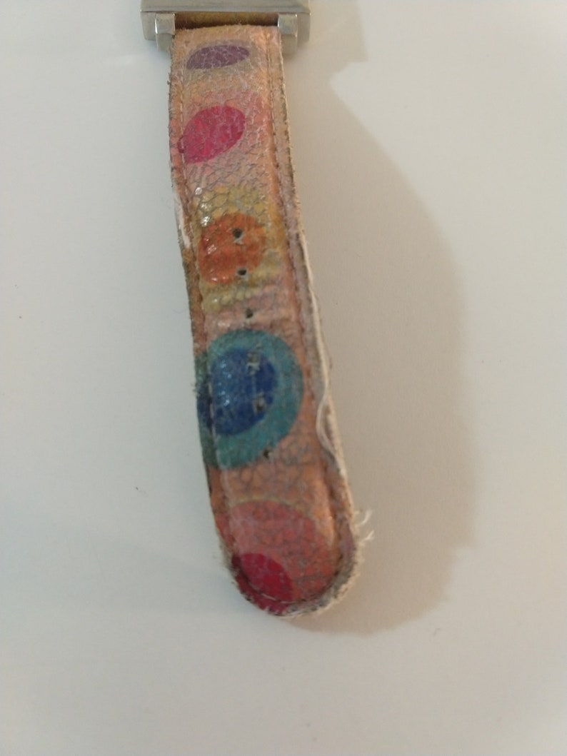 May include: A close-up of a watch strap with a colorful polka dot pattern. The strap is made of leather and has a silver buckle.