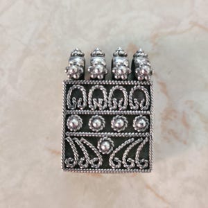May include: A rectangular silver pendant featuring intricate wirework patterns. The top section has four loops with decorative bead accents. The body displays three horizontal bands containing twisted rope motifs, small circular studs, and curved filigree designs.