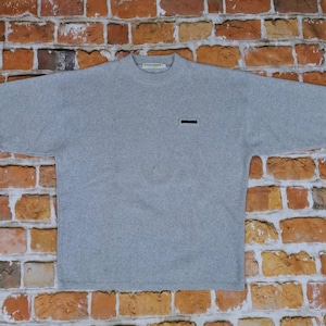 Puede incluir: Una camisa gris de manga larga con un pequeño logotipo negro en el pecho izquierdo.