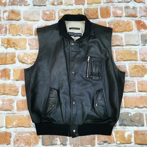 Könnte beinhalten: Schwarze Lederweste mit einer Reißverschlusstasche und einem gerippten Strickbund. Die Weste hat ein Etikett mit der Aufschrift "CHEVRON".