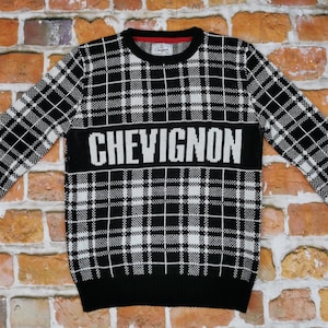 Puede incluir: Jersey de punto de cuadros blanco y negro con la palabra "CHEVIGNON" en letras blancas en el pecho.