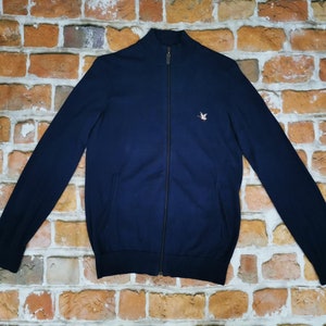 Puede incluir: Un suéter azul marino con cremallera y un pequeño pájaro bordado en el pecho izquierdo.