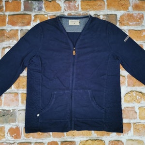 Puede incluir: Chaqueta azul marino con cremallera, mangas largas y bolsillo delantero. La chaqueta tiene un diseño texturizado en la parte delantera y un pequeño logotipo en la manga. La chaqueta tiene cuello en V y cierre de cremallera. La marca es visible en el cuello.