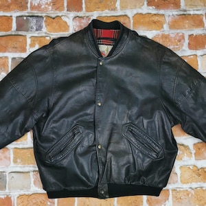 Puede incluir: Una chaqueta bomber de cuero negro con cuello y puños de punto de canalé. La chaqueta tiene cierre de presión y dos bolsillos con cremallera.