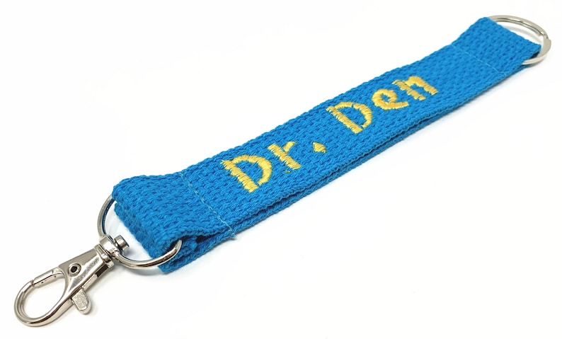 May include: A blue lanyard with a silver swivel hook and a gold embroidered name "Dr. Den".