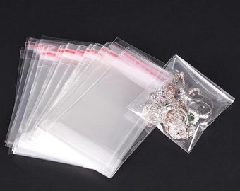 Puede incluir: Una pila de bolsas de plástico transparentes con un sello rojo. Las bolsas son todas del mismo tamaño y son perfectas para empaquetar artículos pequeños. Una bolsa está llena de joyas.