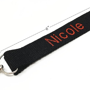 May include: Black fabric key chain with a silver clip and a red embroidered name "Nicole" on it. The key chain is 6 inches long.