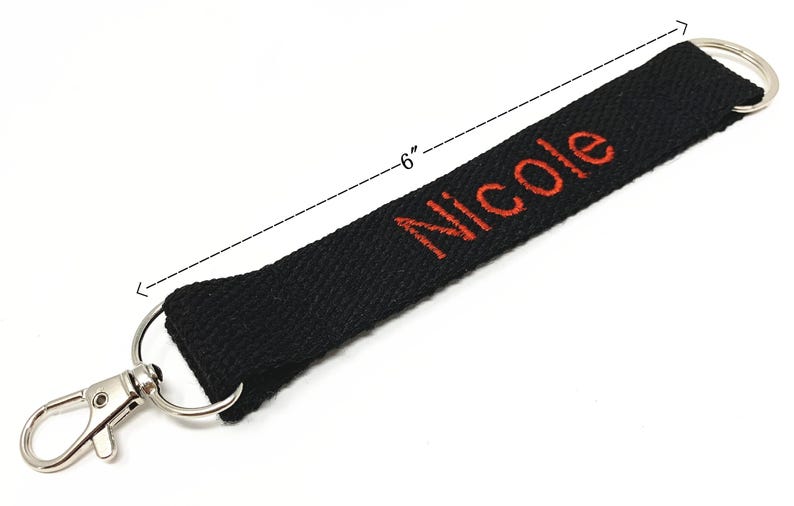 May include: Black fabric key chain with a silver clip and a red embroidered name "Nicole" on it. The key chain is 6 inches long.