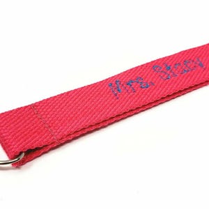 May include: A pink fabric key chain with a silver swivel clip and a blue embroidered inscription that reads "Mrs. Allen".