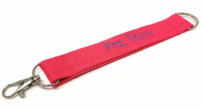 May include: A pink fabric key chain with a silver swivel clip and a blue embroidered inscription that reads "Mrs. Allen".
