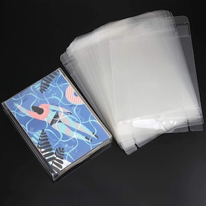 May include: A stack of clear plastic sleeves for protecting cards or photos. The sleeves are made of a clear, flexible plastic and have a flap that folds over to seal the contents. The sleeves are arranged in a stack, with the flap of each sleeve facing outwards. The sleeves are designed to protect cards or photos from damage and dust.