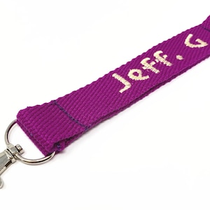 May include: A purple key chain with a silver clip and a ring. The key chain has the name "Jeff. G" embroidered in white.