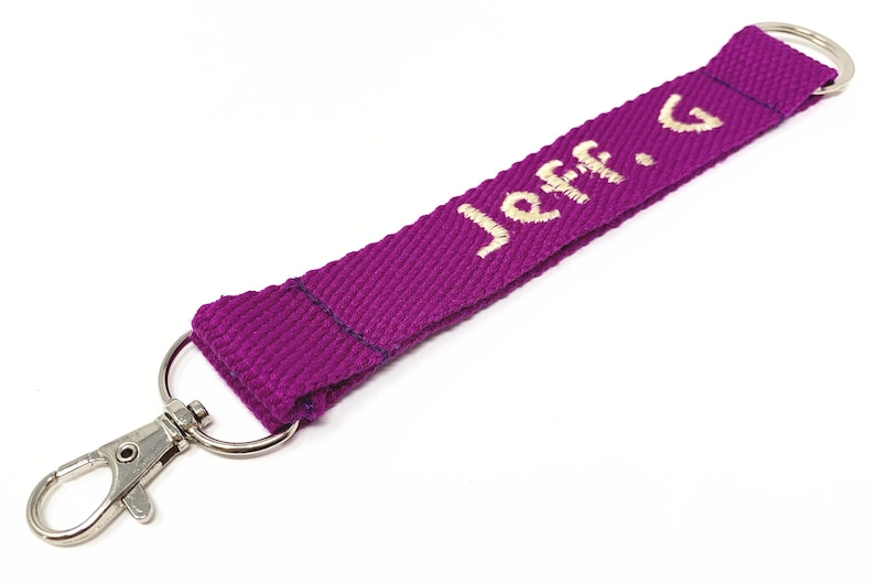 May include: A purple key chain with a silver clip and a ring. The key chain has the name "Jeff. G" embroidered in white.