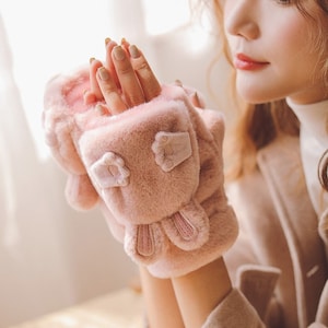 May include: Pink fuzzy bunny fingerless gloves with a white embroidered face. The gloves have a fold-over cuff to keep hands warm.