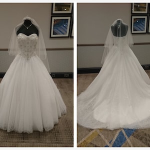 May include: A white wedding dress with a sweetheart neckline and a tulle skirt. The dress has a beaded bodice and a lace trim. The dress is being displayed on a mannequin.