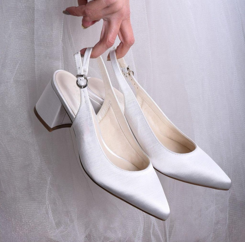 May include: A pair of white satin heeled slingback shoes with a pointed toe.