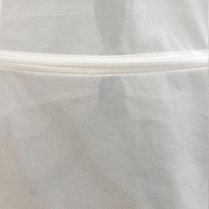 Puede incluir: Bolsa de ropa de malla blanca con una cremallera blanca y un ribete blanco alrededor del borde inferior.