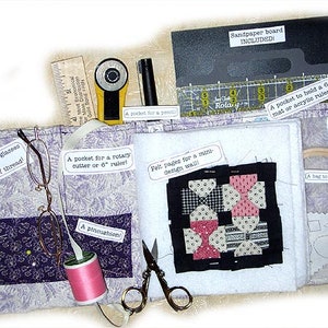 May include: A purple and white fabric project organizer with multiple pockets and compartments. The organizer includes a pincushion, a pocket for glasses or spools of thread, a pocket for a rotary cutter or 6-inch ruler, felt pages for a mini design wall, a pocket to hold a 6-inch mat or acrylic ruler, and a bag to hold anything. The organizer also includes a sandpaper board.