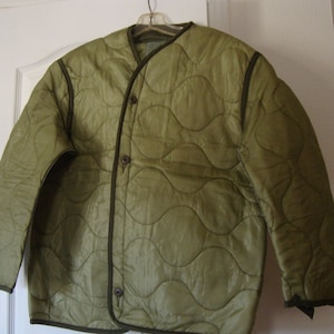 May include: A green quilted jacket with a snap closure and a dark green trim. The jacket is made of a lightweight material and has a relaxed fit.