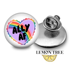May include: A rainbow heart with the text "ALLY AF" on a white background. The heart is on a silver pin back.
