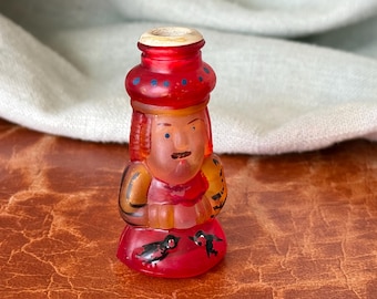 May include: A vintage, hand-painted glass figurine in the shape of a person. The figurine has a red hat with blue dots, an orange face, and a red outfit. Two black birds are painted on the base. The figurine is approximately 3 inches tall.