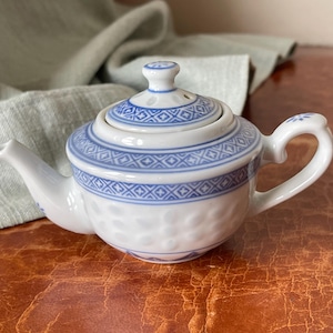 May include: A small white teapot with a blue and white floral design. The teapot has a lid and a spout.