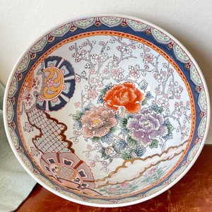 May include: A large white ceramic bowl with a blue, red, and gold floral design. The bowl features a traditional Japanese floral pattern with cherry blossoms and peonies.