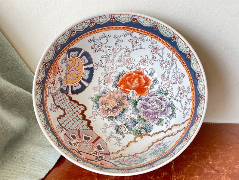 May include: A large white ceramic bowl with a blue, red, and gold floral design. The bowl features a traditional Japanese floral pattern with cherry blossoms and peonies.