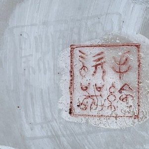 May include: A close-up of a red stamp on a white surface. The stamp contains a series of abstract symbols and characters.