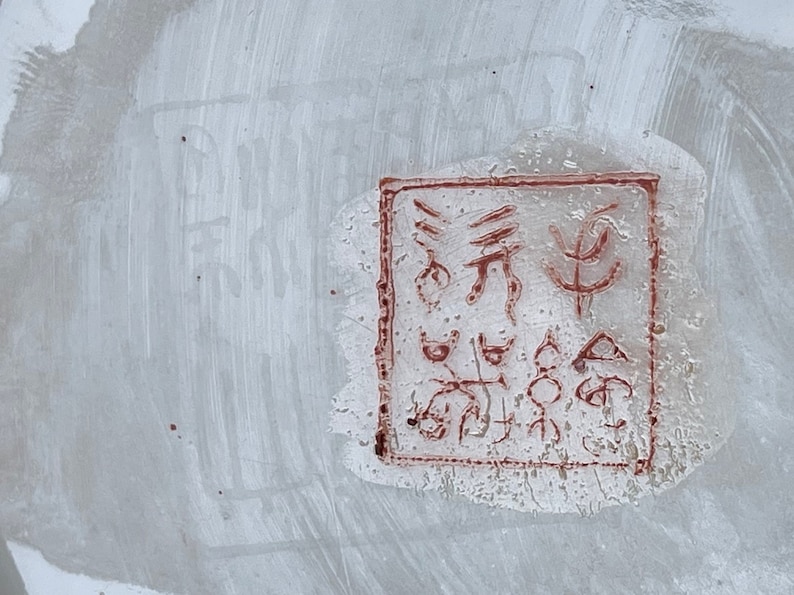 May include: A close-up of a red stamp on a white surface. The stamp contains a series of abstract symbols and characters.
