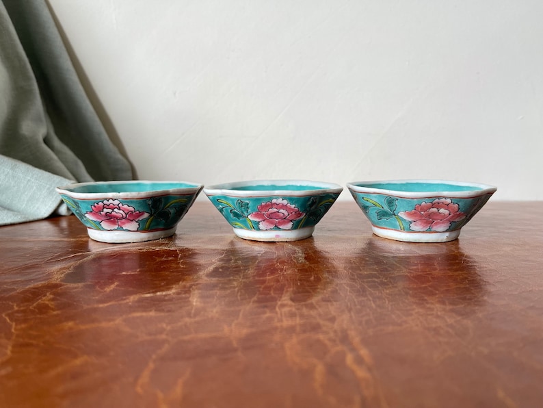 Puede incluir: Tres cuencos peque&ntilde;os de cer&aacute;mica de color turquesa con un borde festoneado. Cada cuenco presenta un dise&ntilde;o floral rosa con hojas verdes.
