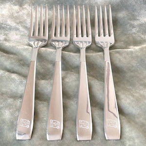 May include: Four silver forks with ornate handles. The forks are arranged in a row, with the handles pointing towards the right.