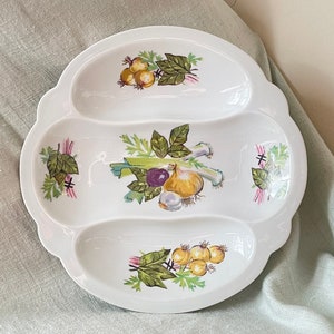 May include: White ceramic serving dish with three sections. Each section features a different painted design of vegetables, including onions, leeks, and tomatoes.