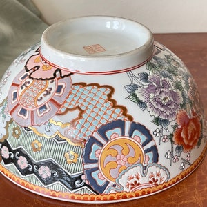 May include: A large white ceramic bowl with a colorful floral and geometric design. The bowl has a wide rim and a rounded bottom. The design features flowers, leaves, and intricate patterns in shades of pink, blue, green, gold, and red.