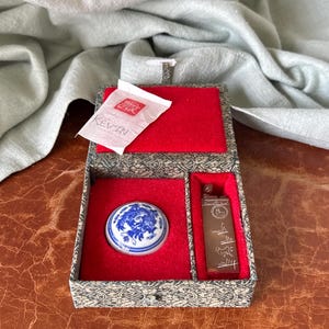 May include: A decorative box with a red velvet interior holds a ceramic seal with a blue and white design, a rectangular seal, and a small packet with the name "KEVIN". The box has a patterned exterior.
