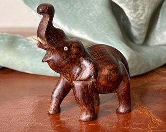 May include: A small, dark brown wooden elephant figurine with ivory tusks. The elephant is standing with its trunk raised in the air.