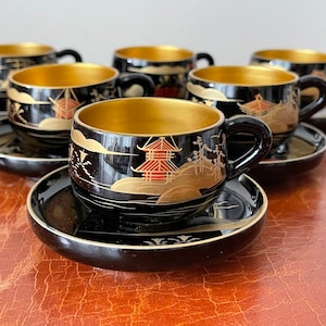 May include: Set of six black and gold teacups and saucers with a Japanese-inspired design. Each cup and saucer features a gold rim and intricate black and gold painted details.
